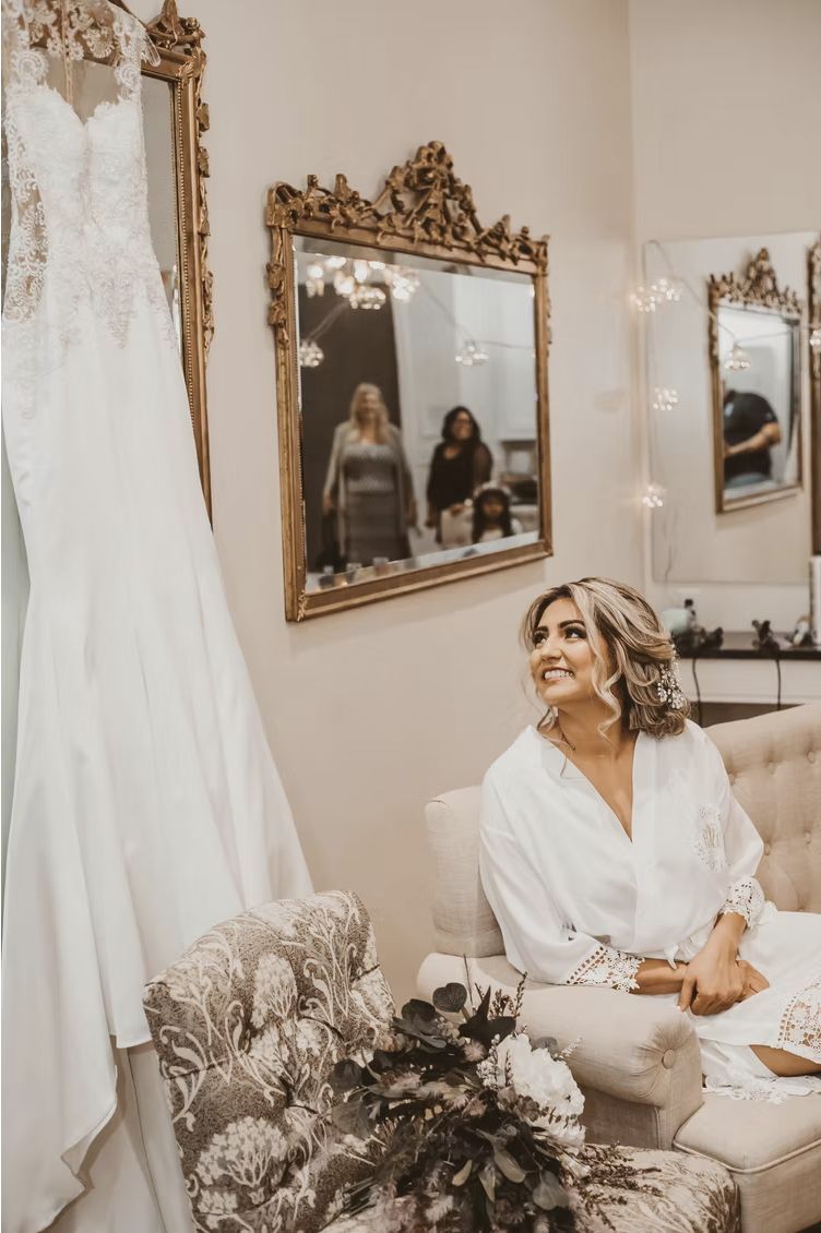 A bride seated in the bridal boutique with her dress hanging beside her