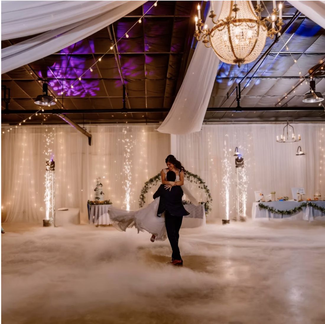 A first dance in fog beneath the chandelier and string lights