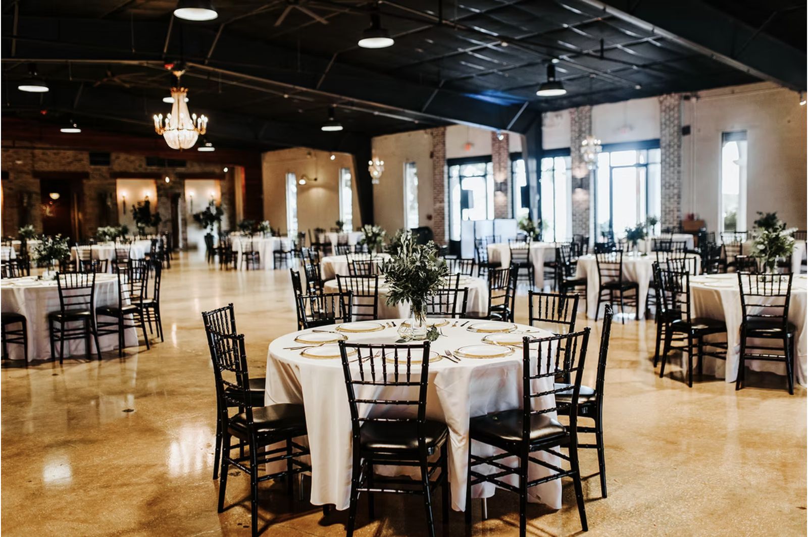 The hall at Venue 650 set with round tables and black chiavari chairs under a dark exposed ceiling