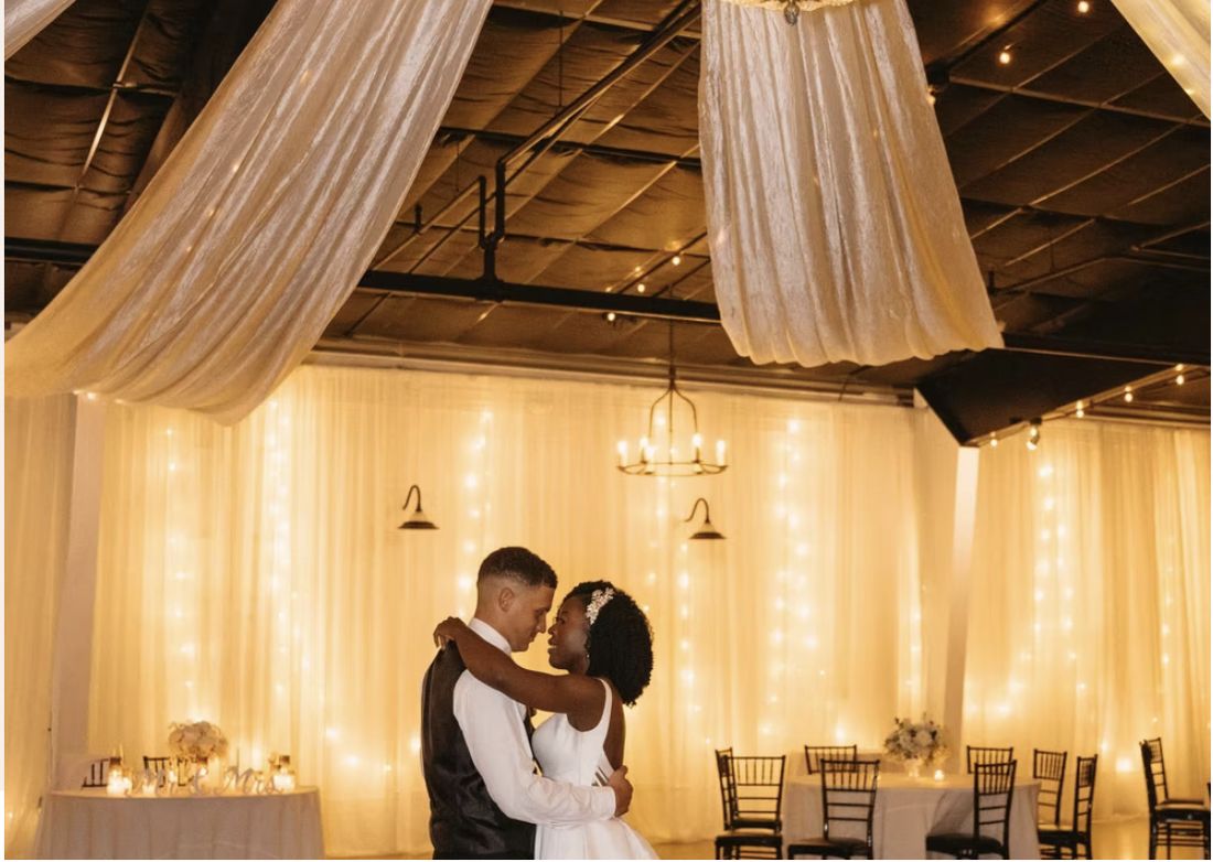 A couple beneath warm drapery and string lights at Venue 650